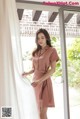 a woman standing in front of a window wearing a pink dress
