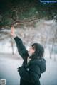 A woman in a black jacket reaching up to a tree.