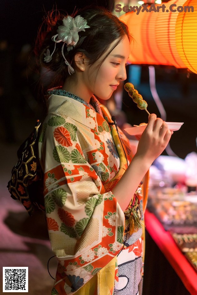 A woman in a kimono eating a piece of food.