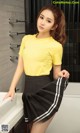 A woman in a yellow shirt and black skirt posing for a picture.