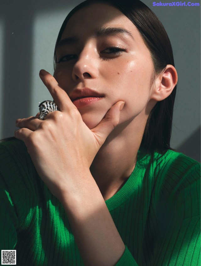 A woman wearing a green sweater and a silver ring.