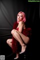 A woman with pink hair sitting on a stool.