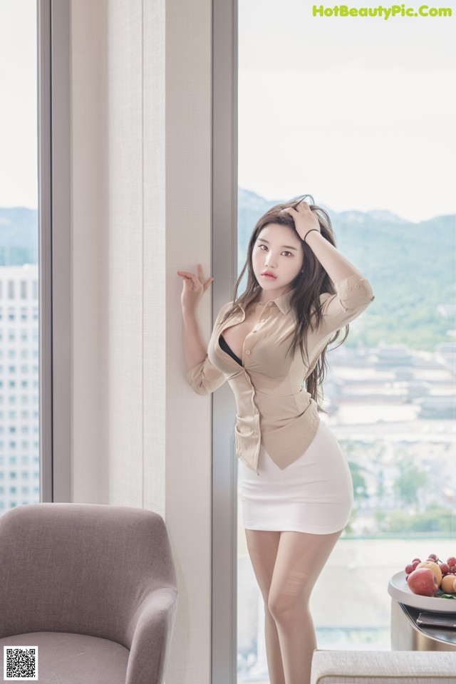A woman standing in front of a window next to a chair.