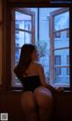 A woman in a black bodysuit sitting by a window.