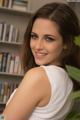 A woman in a white tank top sitting in front of a book shelf.